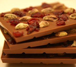 A stack of four belgian chocolate bars with cranberries and pistachios sprinkle on top of each bar